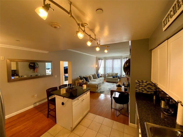 kitchen with a kitchen breakfast bar, crown molding, dark countertops, open floor plan, and white cabinetry