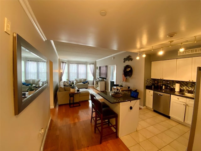 kitchen with dark countertops, a breakfast bar, ornamental molding, stainless steel dishwasher, and a kitchen island