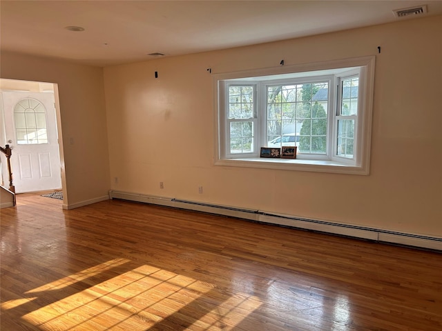 unfurnished room featuring baseboards, visible vents, wood finished floors, and a baseboard heating unit