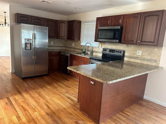 kitchen with light stone counters, light wood-style flooring, a sink, stainless steel appliances, and a peninsula