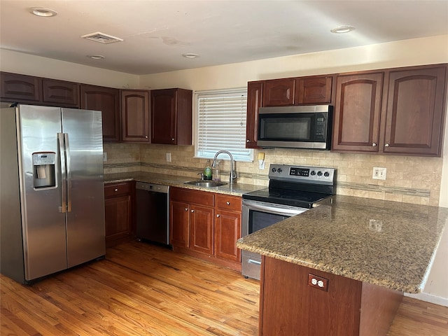 kitchen featuring appliances with stainless steel finishes, stone counters, a sink, visible vents, and a peninsula