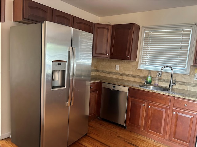 kitchen featuring light stone countertops, a sink, stainless steel appliances, decorative backsplash, and wood finished floors