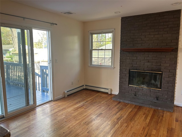 unfurnished living room with a brick fireplace, visible vents, baseboards, baseboard heating, and wood finished floors