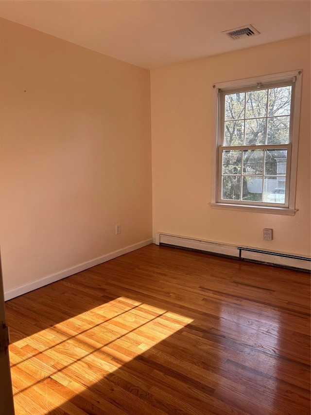 spare room with wood finished floors, visible vents, a baseboard heating unit, and baseboards