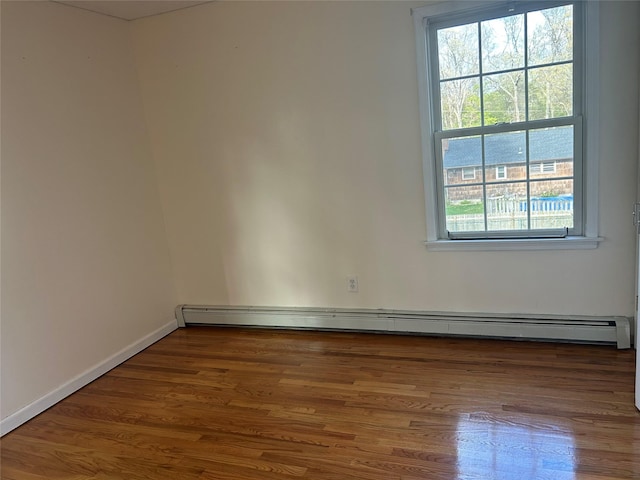 empty room with a baseboard heating unit, wood finished floors, and baseboards