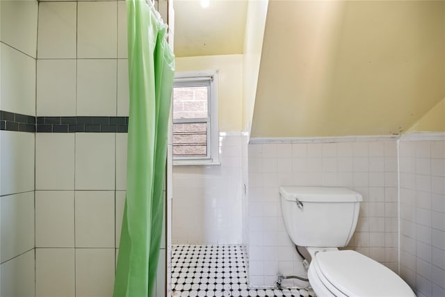 full bath featuring toilet, a shower with curtain, wainscoting, and tile walls