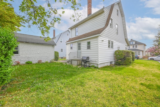rear view of house featuring a lawn, roof with shingles, and a chimney