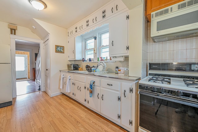 kitchen featuring light countertops, white microwave, decorative backsplash, and range with gas cooktop