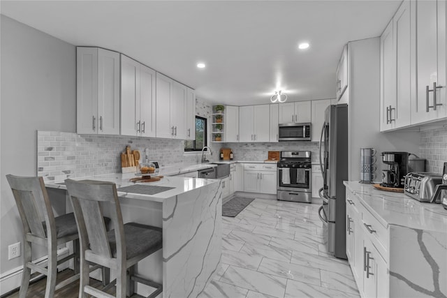 kitchen featuring stainless steel appliances, tasteful backsplash, white cabinetry, a peninsula, and light stone counters