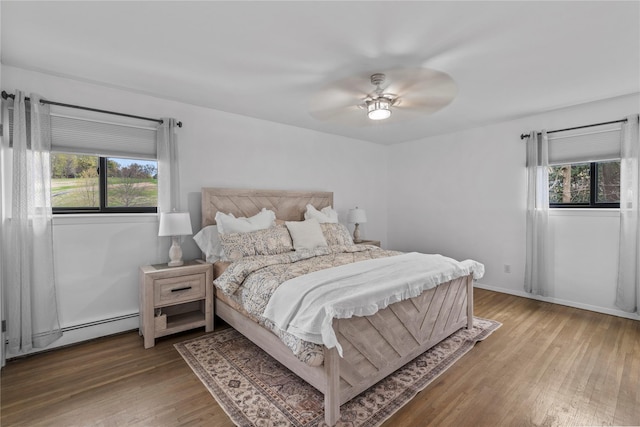 bedroom featuring light wood-style floors, ceiling fan, a baseboard heating unit, and multiple windows