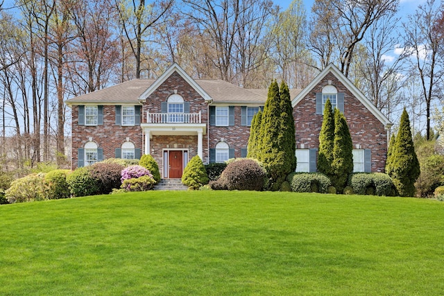 georgian-style home with a front yard, brick siding, and a balcony