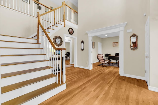 stairs with baseboards, wood finished floors, and a high ceiling