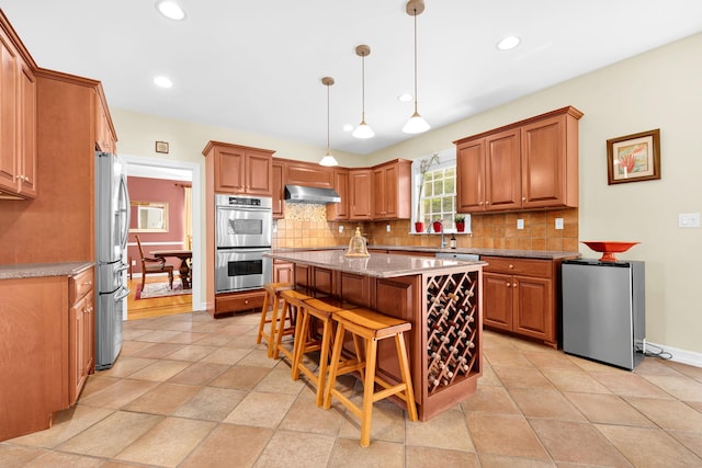 kitchen with appliances with stainless steel finishes, tasteful backsplash, a kitchen breakfast bar, and under cabinet range hood