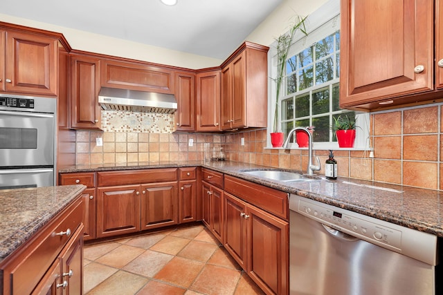 kitchen with ventilation hood, stainless steel appliances, dark stone counters, and a sink