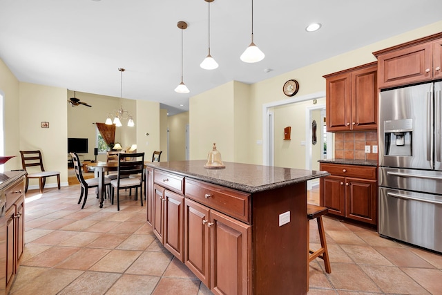 kitchen with dark stone counters, backsplash, a center island, stainless steel refrigerator with ice dispenser, and hanging light fixtures