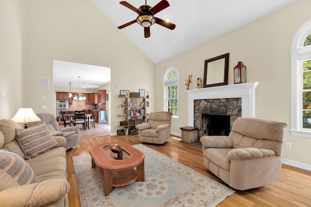 living room with ceiling fan, baseboards, light wood-type flooring, high vaulted ceiling, and a stone fireplace