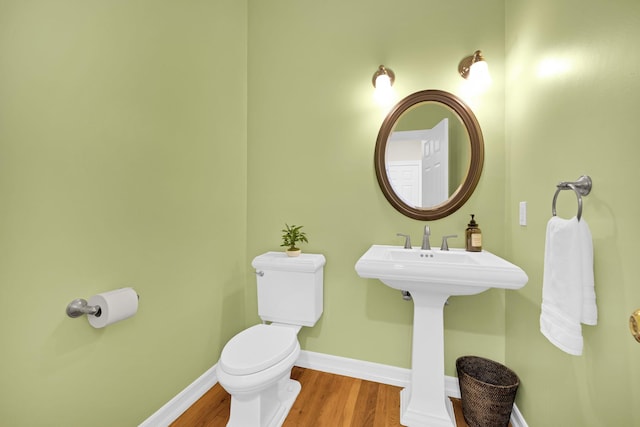 half bath with toilet, wood finished floors, and baseboards