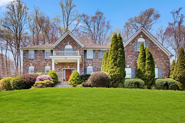 colonial-style house featuring brick siding, a balcony, and a front yard