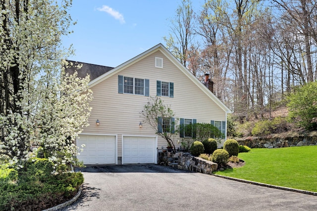 view of property exterior with a chimney, a yard, aphalt driveway, roof with shingles, and an attached garage