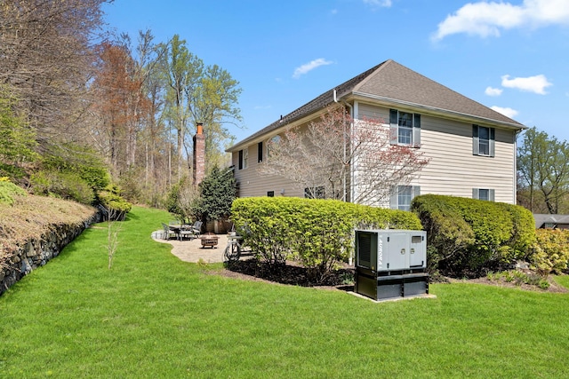 view of side of property with an outdoor fire pit, a shingled roof, and a lawn