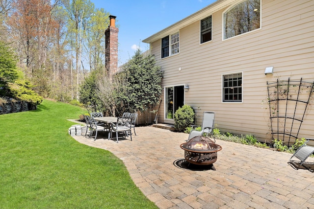 back of property featuring a lawn, a patio, a chimney, and an outdoor fire pit