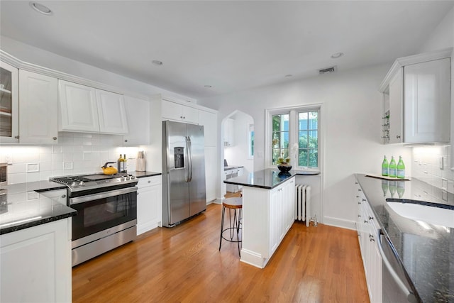 10 Maple Hill Dr, Larchmont, NY 10538 - kitchen with stainless steel appliances, radiator heating unit, a peninsula, arched walkways, and white cabinetry