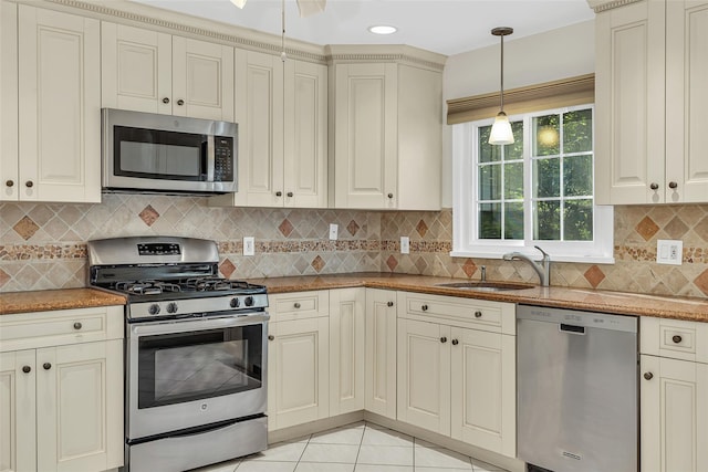 kitchen with a sink, cream cabinets, decorative light fixtures, backsplash, and appliances with stainless steel finishes