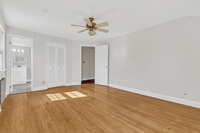unfurnished bedroom with a closet, baseboards, light wood-type flooring, a ceiling fan, and ensuite bath