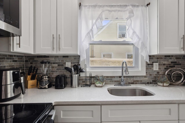 kitchen featuring stainless steel microwave, backsplash, white cabinetry, and a sink