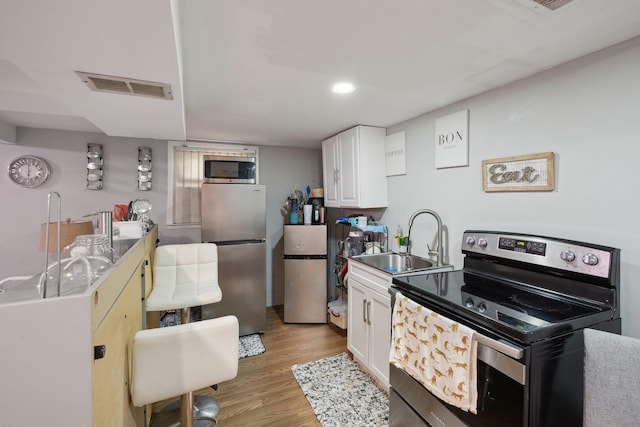 kitchen with appliances with stainless steel finishes, light wood finished floors, a sink, white cabinetry, and visible vents