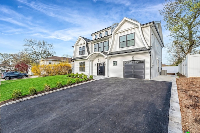 shingle-style home with fence, an attached garage, a front yard, central AC unit, and driveway