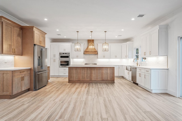 kitchen with custom range hood, decorative backsplash, light wood-style floors, and stainless steel appliances