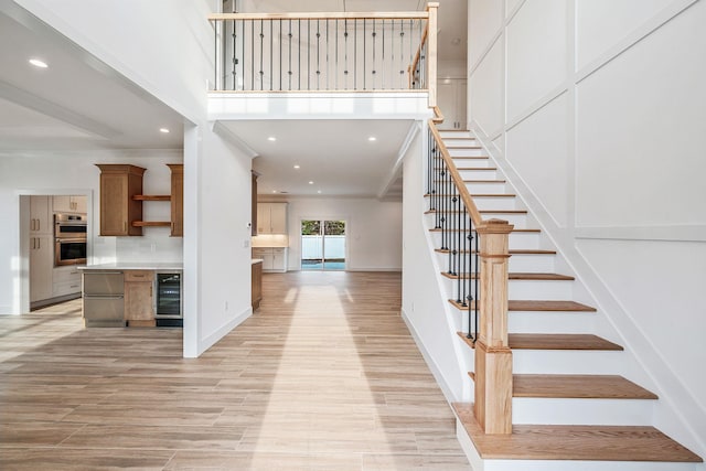 stairway featuring wood finished floors, baseboards, beverage cooler, a high ceiling, and recessed lighting