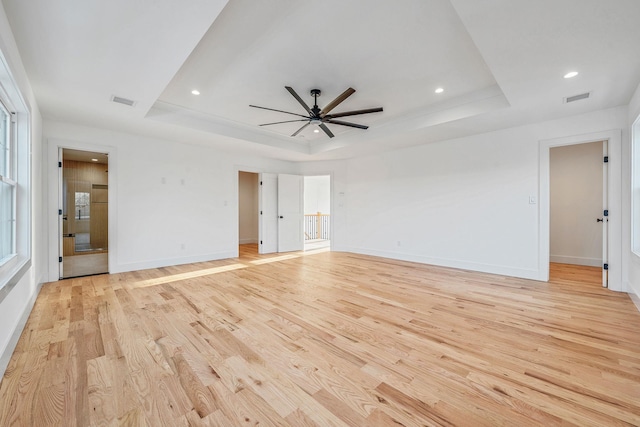 interior space featuring baseboards, a tray ceiling, visible vents, and light wood-style flooring