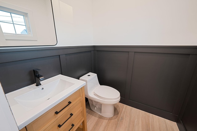 bathroom featuring wood finished floors, vanity, a wainscoted wall, toilet, and a decorative wall