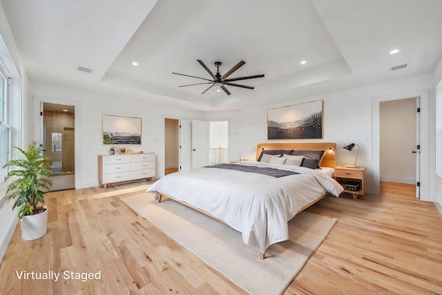 bedroom with a tray ceiling, recessed lighting, light wood-style flooring, and visible vents