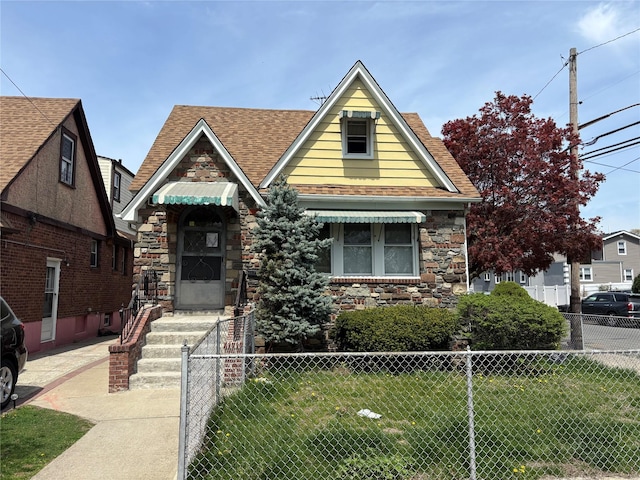 view of front facade featuring fence, a shingled roof, a front lawn, and stone siding