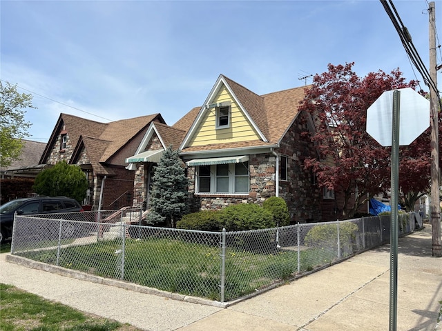 view of front facade featuring a fenced front yard, a shingled roof, stone siding, and a front lawn