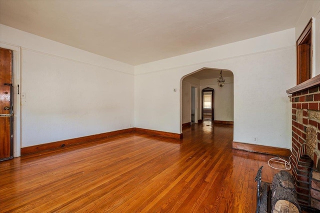 unfurnished living room featuring arched walkways, baseboards, and wood finished floors