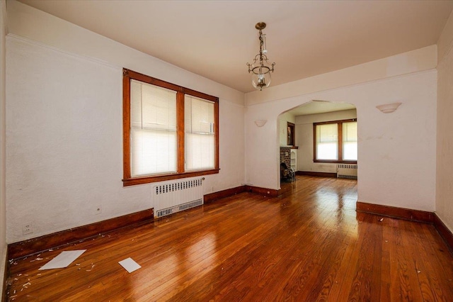 unfurnished room with radiator, hardwood / wood-style flooring, baseboards, and arched walkways