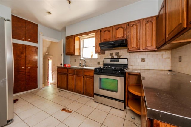 kitchen featuring brown cabinetry, under cabinet range hood, tasteful backsplash, a sink, and appliances with stainless steel finishes