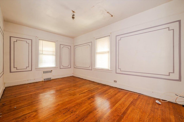 empty room featuring light wood-style floors, baseboards, radiator heating unit, and a healthy amount of sunlight