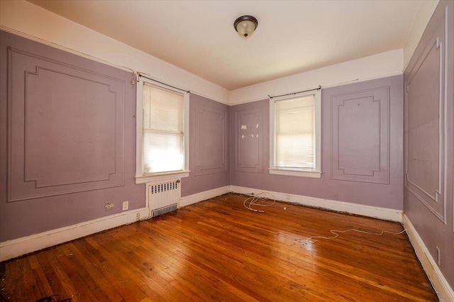 empty room featuring wood-type flooring, baseboards, and radiator heating unit