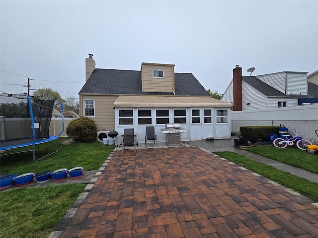 rear view of house with a chimney, a trampoline, a fenced backyard, a yard, and a patio area