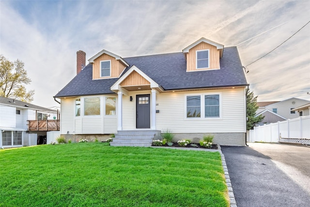 view of front of house with fence, roof with shingles, a chimney, and a front lawn