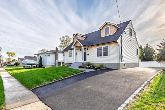 view of front of property featuring a front lawn, fence, a shingled roof, and aphalt driveway