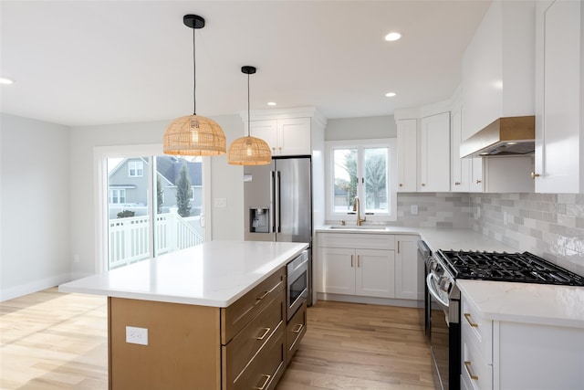 kitchen with a sink, stainless steel appliances, light wood-style floors, a center island, and wall chimney range hood