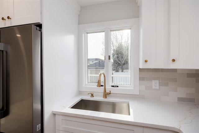 kitchen with light stone counters, white cabinetry, tasteful backsplash, a sink, and freestanding refrigerator