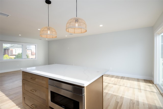kitchen featuring stainless steel microwave, light wood-style floors, a center island, visible vents, and baseboards