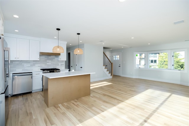 kitchen with stainless steel appliances, a kitchen island, white cabinets, backsplash, and light wood-type flooring